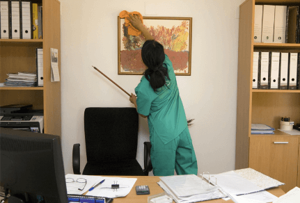 Cleaning professional in an office dusting painting on wall